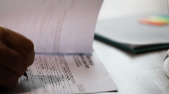 Person Filling Out Documents at a Desk with Passports and Hourglass-Shutterstock_2586825645