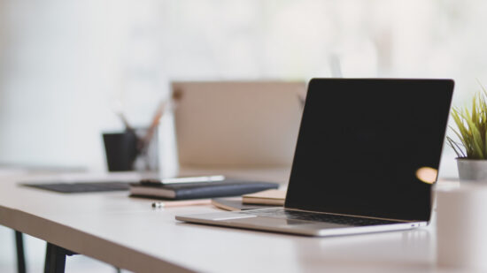 Open blank laptop in modern workplace with office supplies and decorations on white table